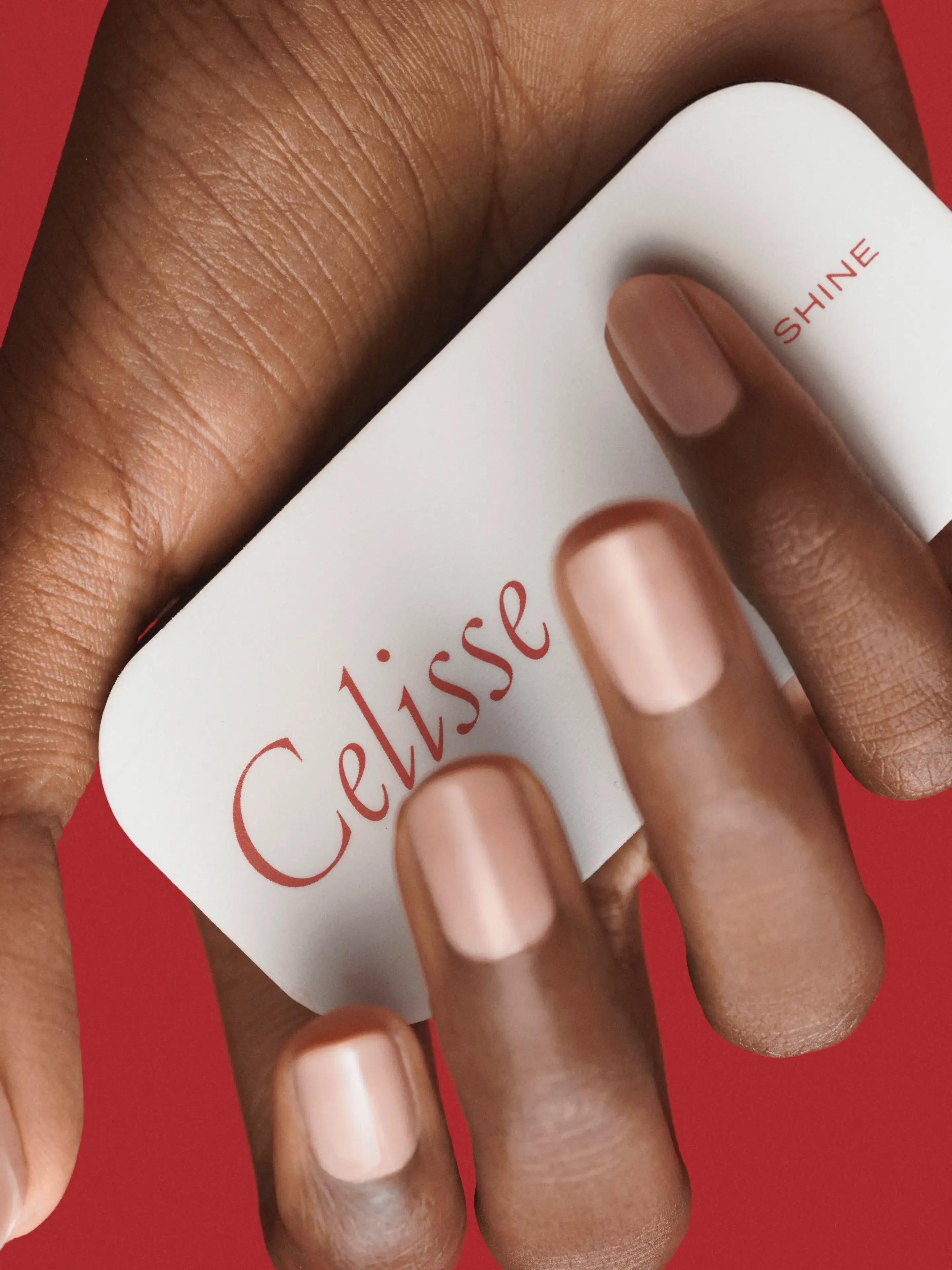 Hand holding a white buffer with 'Celisse' and 'Shine' text against a red background